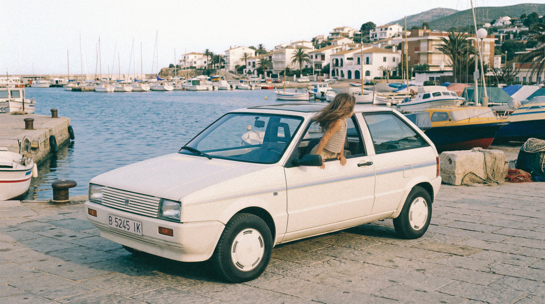 SEAT Ibiza blanco en un puerto con una niña asomada por la ventanilla